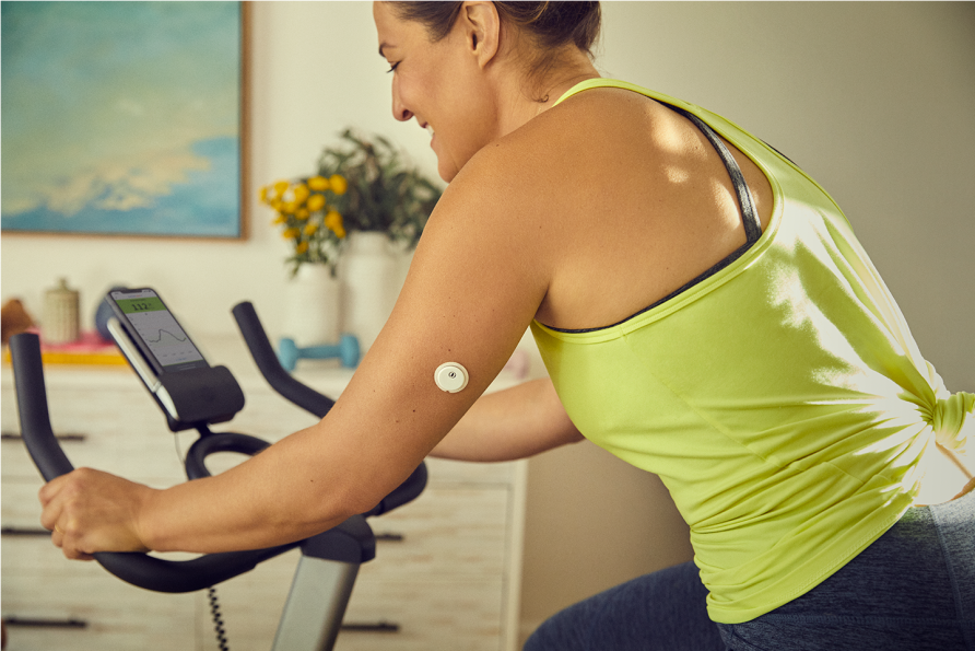 Woman wearing a glucose sensor while exercising on a stationary bike